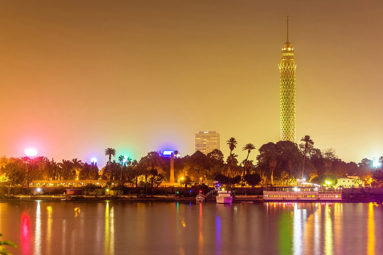 Nighttime view of a cityscape with a tall illuminated tower by the river.